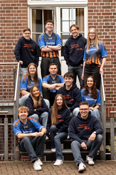 12 Junge Menschen sitzen hintereinander in Volksbank Trikots auf einer Treppe
